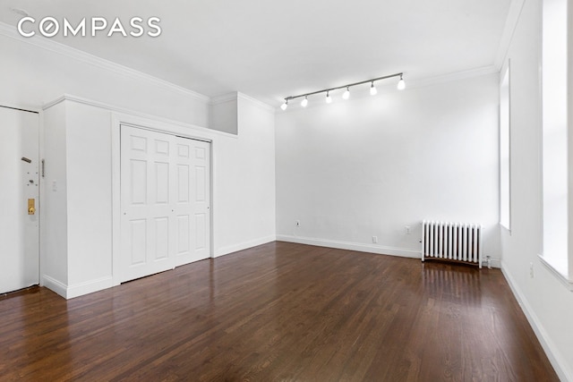 unfurnished bedroom with track lighting, crown molding, radiator, and dark wood-style floors