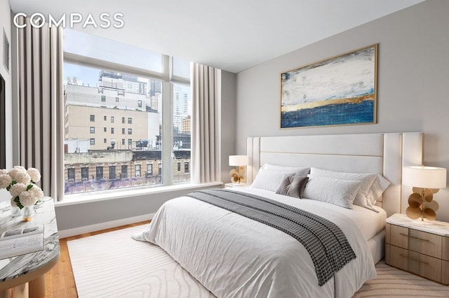 bedroom with a city view, baseboards, and light wood-type flooring