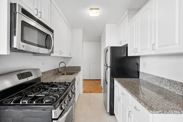 kitchen with appliances with stainless steel finishes, a sink, white cabinets, and stone countertops