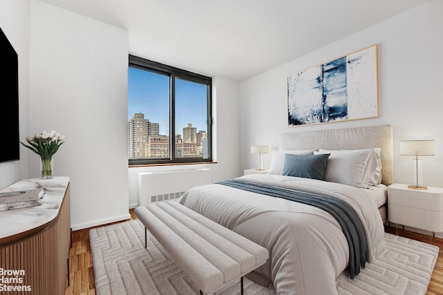 bedroom with wood finished floors, radiator, a skyline view, and baseboards