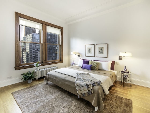 bedroom with radiator heating unit, baseboards, and wood finished floors