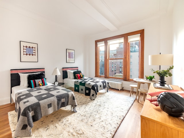 bedroom with light wood-type flooring, baseboards, radiator heating unit, and beamed ceiling