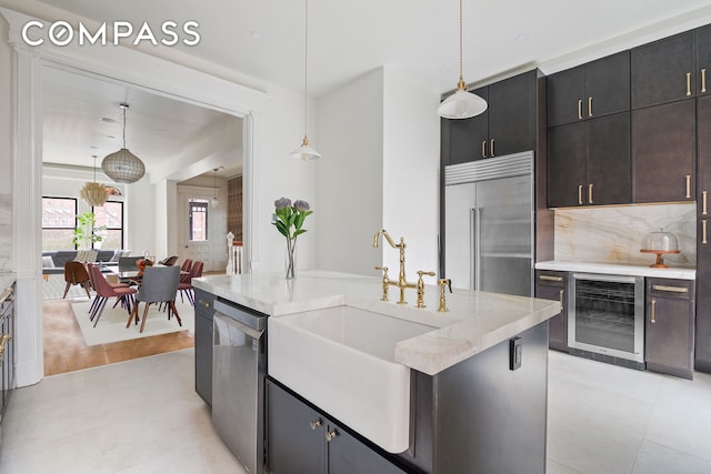 kitchen with decorative light fixtures, a sink, light stone counters, wine cooler, and stainless steel appliances