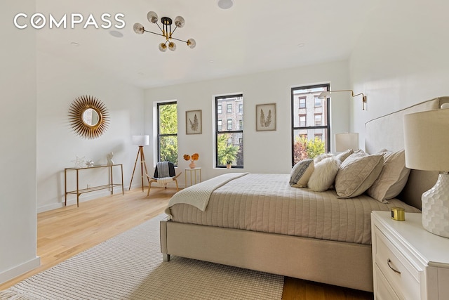 bedroom with baseboards, light wood finished floors, and a notable chandelier