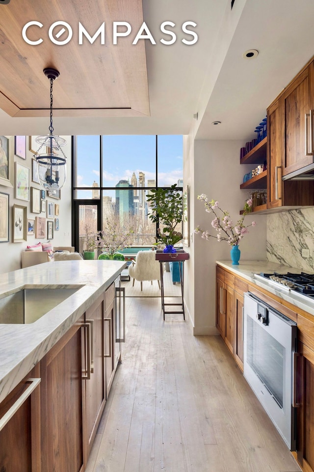 90 Furman St Unit N510, New York City, NY 11201 - kitchen featuring brown cabinetry, tasteful backsplash, light wood finished floors, light stone counters, and stainless steel gas cooktop