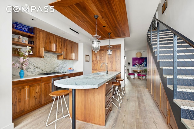 90 Furman St Unit N510, New York City, NY 11201 - kitchen with brown cabinets, light wood-style flooring, backsplash, a kitchen breakfast bar, and stainless steel gas stovetop