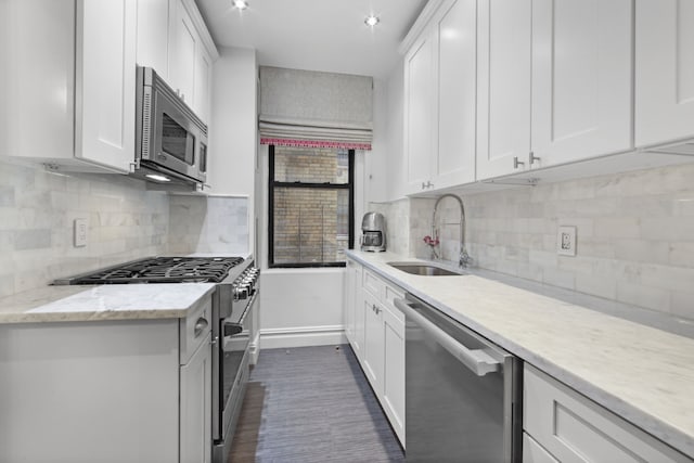 kitchen with appliances with stainless steel finishes, a sink, baseboards, tasteful backsplash, and white cabinetry