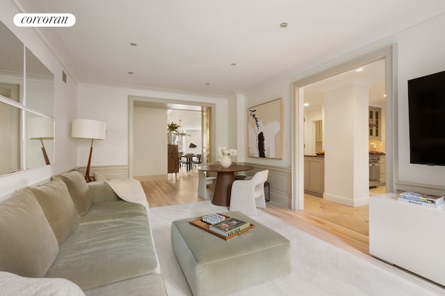 living room featuring light wood-type flooring, wainscoting, ornamental molding, a decorative wall, and recessed lighting