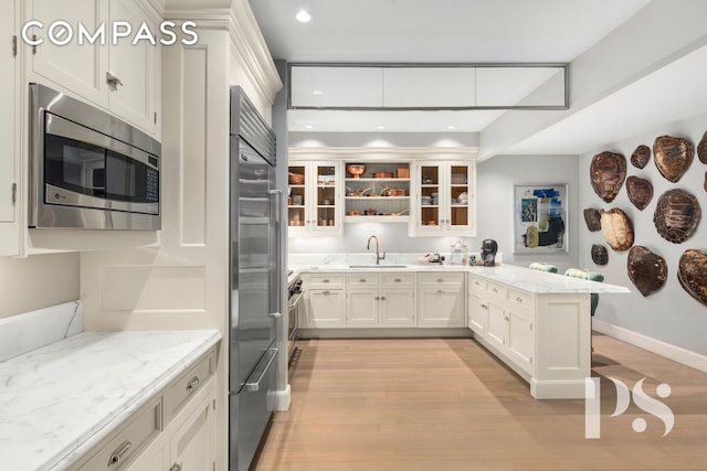 135 E 79th St Unit 8E, New York City, NY 10075 - kitchen with appliances with stainless steel finishes, a sink, a peninsula, light wood-style floors, and glass insert cabinets