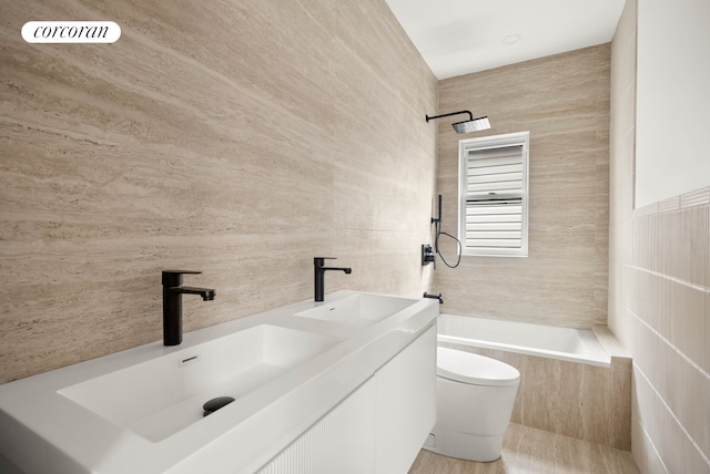 full bath featuring a sink, tile walls, tiled shower / bath, and toilet
