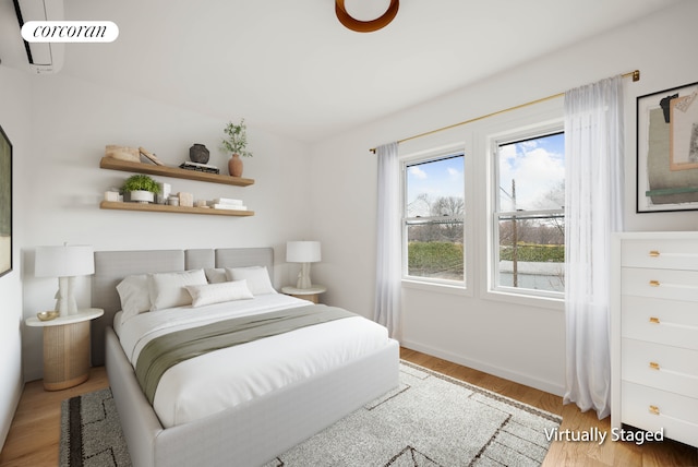 bedroom with baseboards, a wall unit AC, and wood finished floors