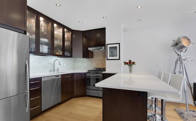 kitchen with appliances with stainless steel finishes, a sink, a peninsula, under cabinet range hood, and a kitchen breakfast bar
