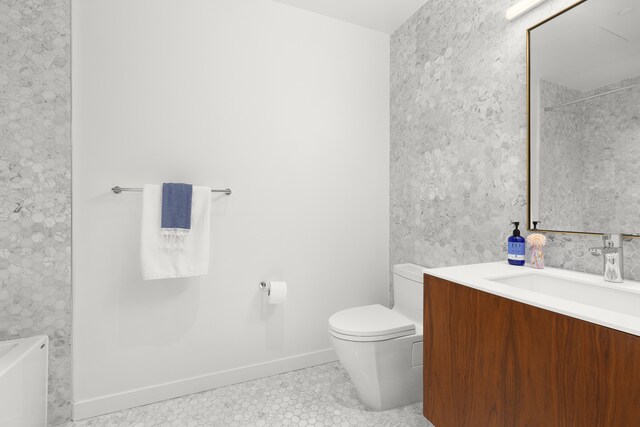 bathroom featuring tile patterned flooring, vanity, toilet, baseboards, and a bath