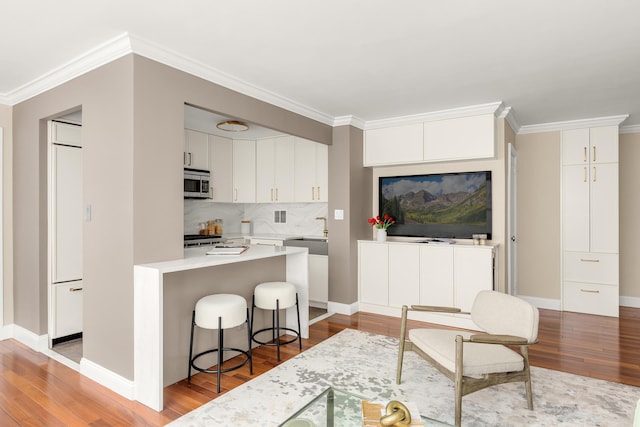 kitchen featuring stainless steel microwave, light wood-style floors, a sink, white cabinets, and crown molding