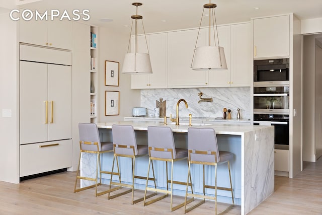 100 W 80th St Unit 5B, New York City, NY 10024 - kitchen featuring paneled built in refrigerator, light wood finished floors, decorative backsplash, and an island with sink