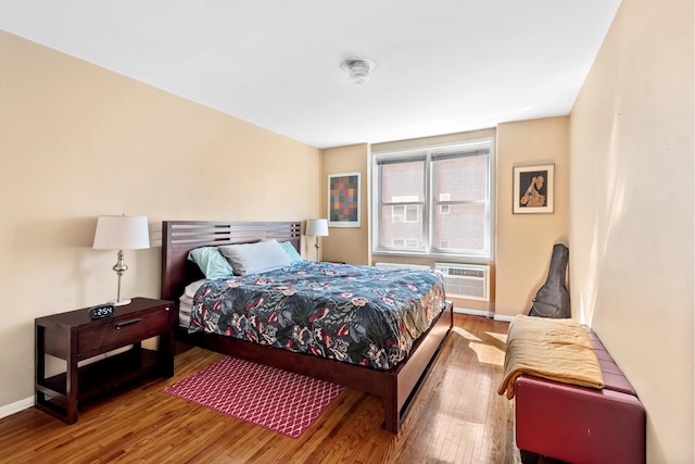 bedroom with baseboards, wood finished floors, and a wall mounted AC