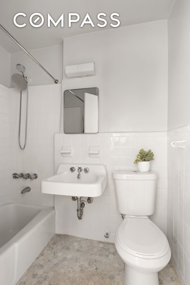 full bath featuring tile walls, toilet, shower / washtub combination, and a sink