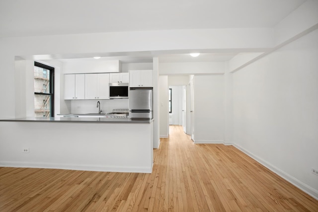4489 Broadway Unit 5E, New York City, NY 10040 - kitchen featuring white cabinets, light wood finished floors, freestanding refrigerator, a peninsula, and dark countertops