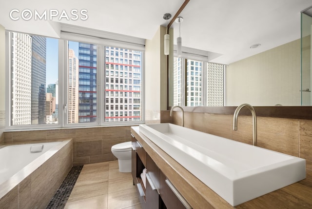 full bathroom featuring a city view, tile walls, toilet, tiled bath, and vanity