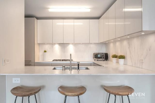 kitchen featuring a sink, modern cabinets, a peninsula, and backsplash