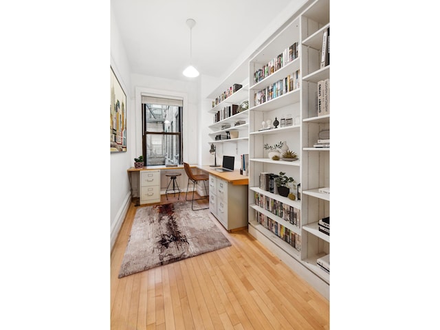 office with built in desk, baseboards, and light wood-style flooring