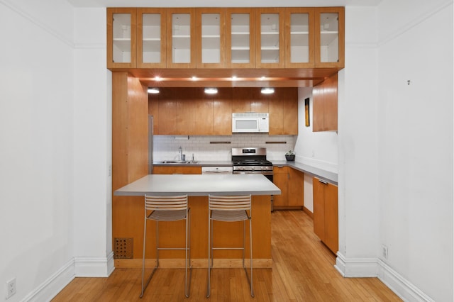 kitchen with white microwave, light wood-style flooring, a peninsula, and stainless steel gas stove