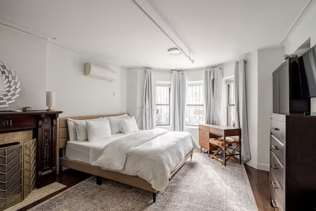 bedroom featuring a tile fireplace, an AC wall unit, and wood finished floors
