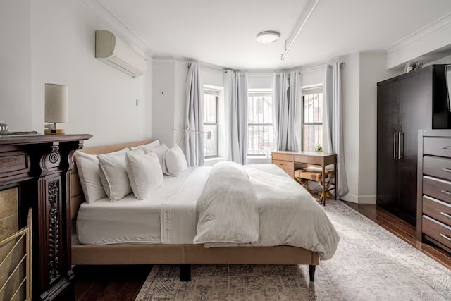 bedroom featuring a wall mounted AC, dark wood-style floors, baseboards, and crown molding