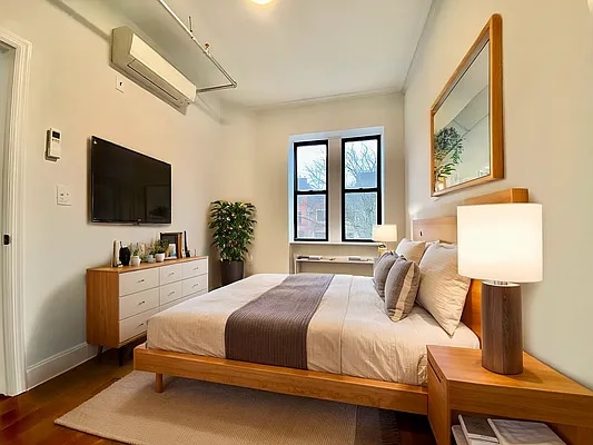 bedroom featuring wood finished floors, baseboards, and an AC wall unit