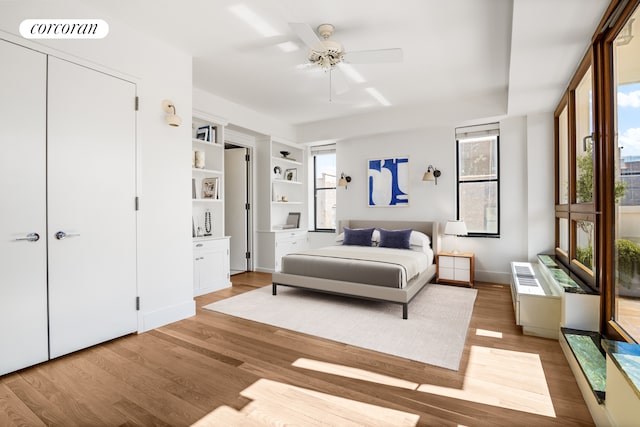 bedroom with multiple windows, light wood-type flooring, baseboards, and a ceiling fan