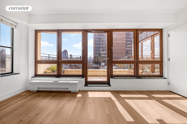 empty room featuring wood finished floors, plenty of natural light, baseboards, and radiator
