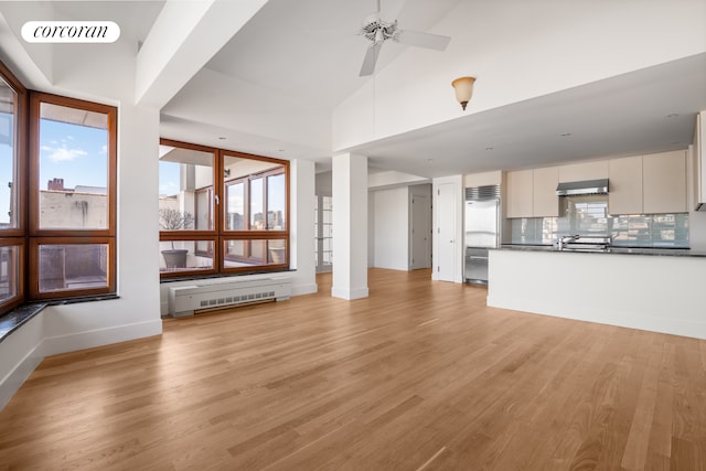 unfurnished living room with light wood-style floors, ceiling fan, baseboards, radiator heating unit, and vaulted ceiling