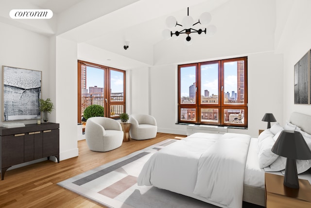 bedroom with a skyline view, wood finished floors, a chandelier, high vaulted ceiling, and baseboards