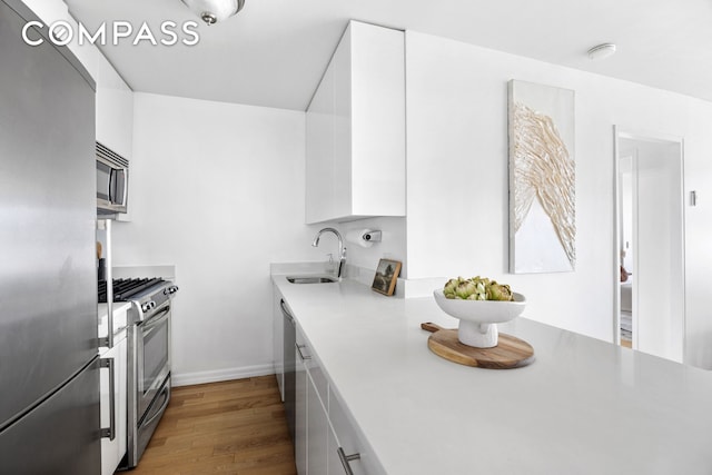 kitchen with appliances with stainless steel finishes, wood finished floors, a sink, light countertops, and white cabinets