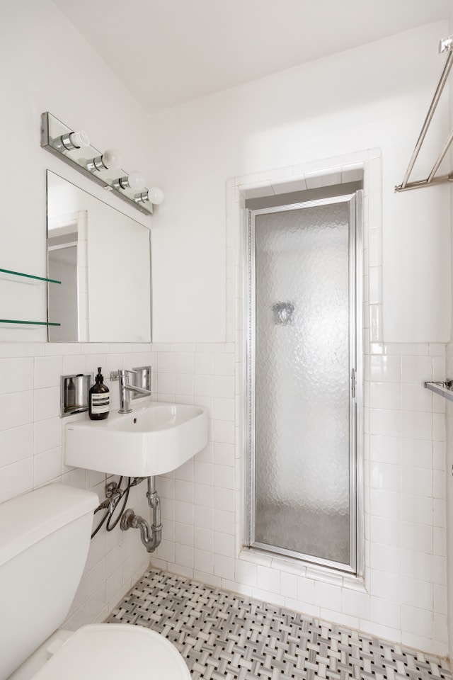 140 7th Ave Unit 4L, New York City, NY 10011 - bathroom featuring tile walls, a shower stall, and wainscoting
