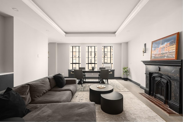 living room featuring a raised ceiling, wood finished floors, a fireplace, baseboards, and ornamental molding