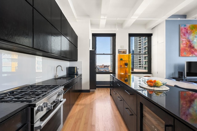 448 W 37th St Unit 9A, New York City, NY 10018 - kitchen featuring gas range, dark cabinets, light wood-style floors, dark countertops, and beamed ceiling