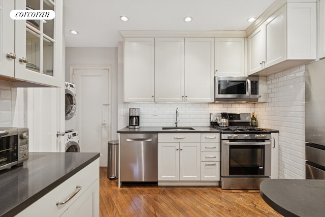 240 W 98th St Unit 3D, New York City, NY 10025 - kitchen featuring appliances with stainless steel finishes, a sink, stacked washer and clothes dryer, dark countertops, and light wood-style flooring