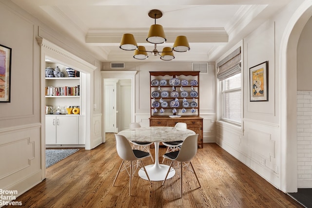 dining space with arched walkways, light wood finished floors, a chandelier, crown molding, and a decorative wall