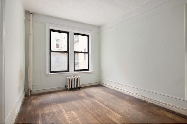 spare room with radiator heating unit, hardwood / wood-style flooring, baseboards, and a textured ceiling