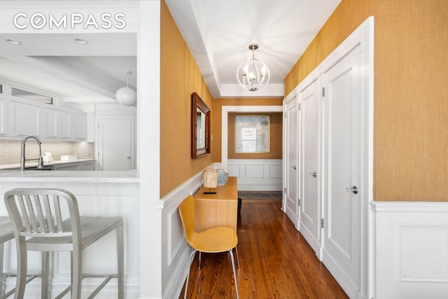 hallway featuring a sink, a chandelier, dark wood-type flooring, a decorative wall, and wainscoting