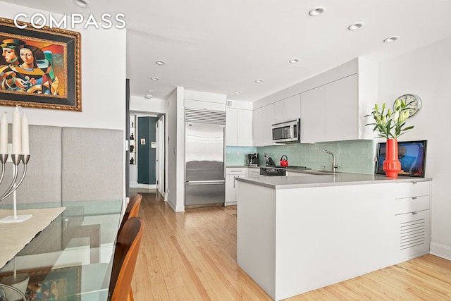 kitchen with stainless steel appliances, light wood-style floors, a peninsula, white cabinets, and a sink
