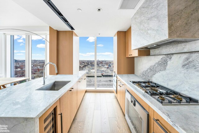 50 Bridge Park Dr Unit 21D, New York City, NY 11201 - kitchen featuring wall chimney exhaust hood, a sink, stainless steel gas cooktop, oven, and light wood finished floors