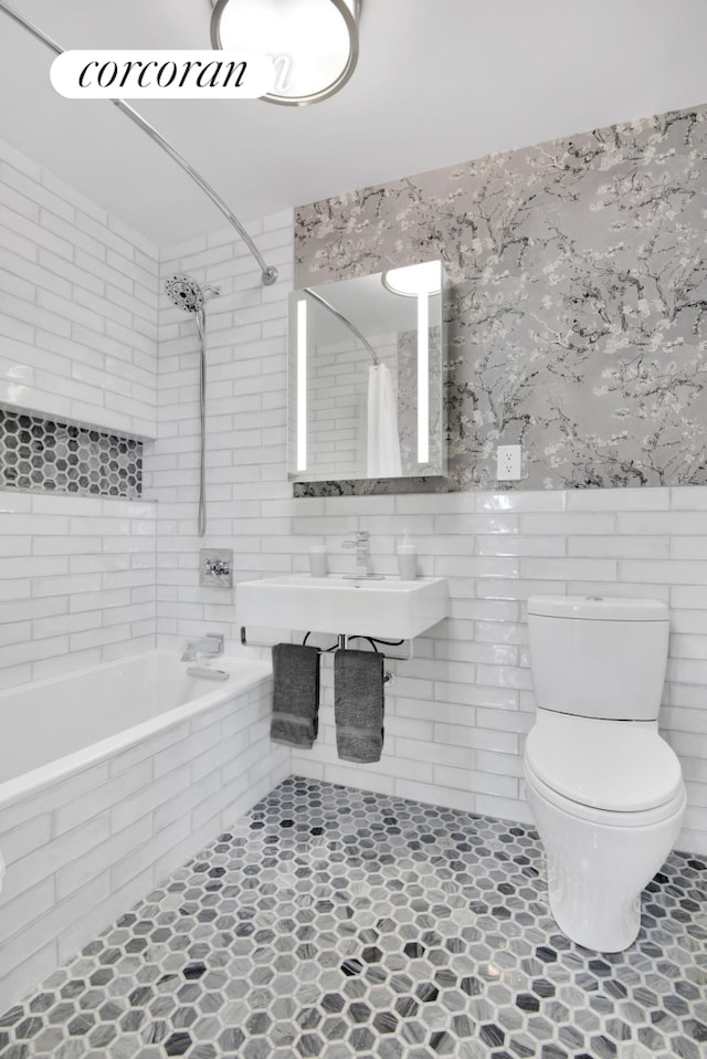 full bathroom featuring tile patterned flooring, tiled shower / bath, toilet, a sink, and tile walls