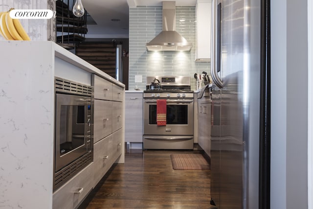 kitchen featuring backsplash, modern cabinets, dark wood-type flooring, wall chimney exhaust hood, and appliances with stainless steel finishes