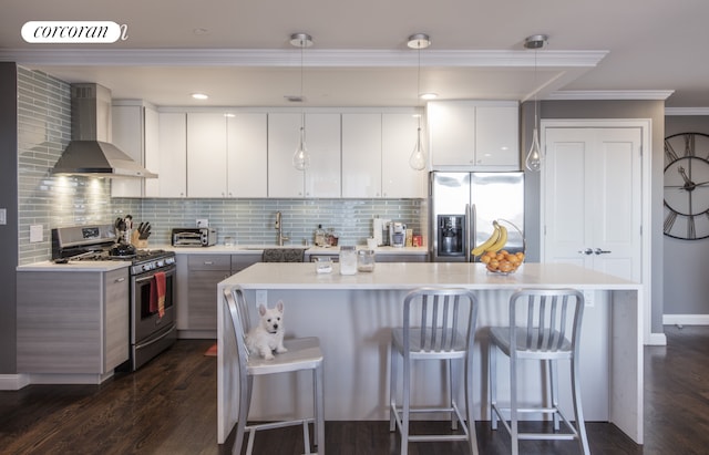kitchen with a sink, a breakfast bar, light countertops, wall chimney exhaust hood, and appliances with stainless steel finishes