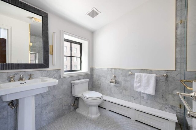 241 E 48th St, New York City, NY 10017 - bathroom featuring visible vents, toilet, tile walls, a baseboard radiator, and tile patterned floors
