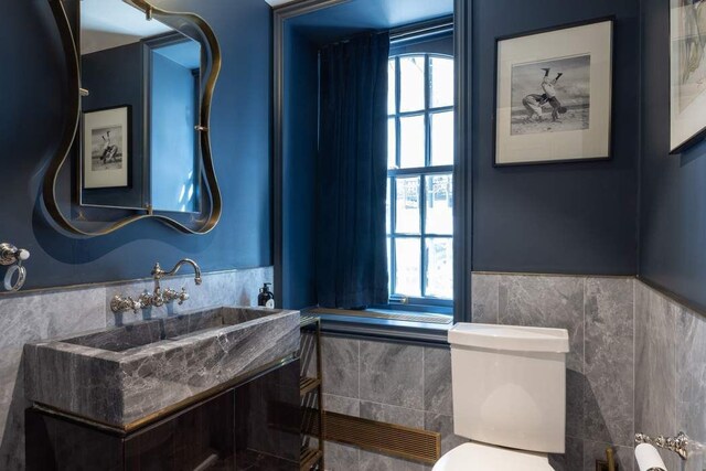 241 E 48th St, New York City, NY 10017 - half bathroom featuring tile walls, toilet, a wainscoted wall, and a wealth of natural light