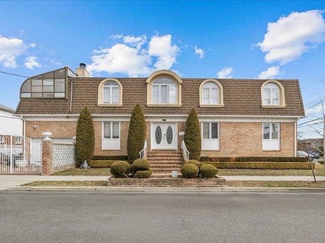 view of front of house with a chimney, mansard roof, fence, and brick siding