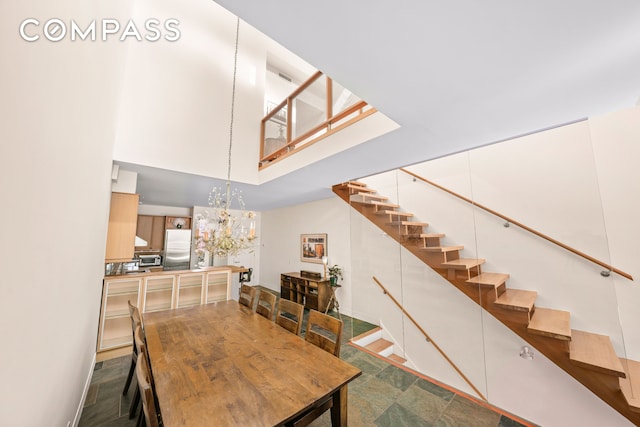 dining area featuring stairway, baseboards, an inviting chandelier, and a towering ceiling